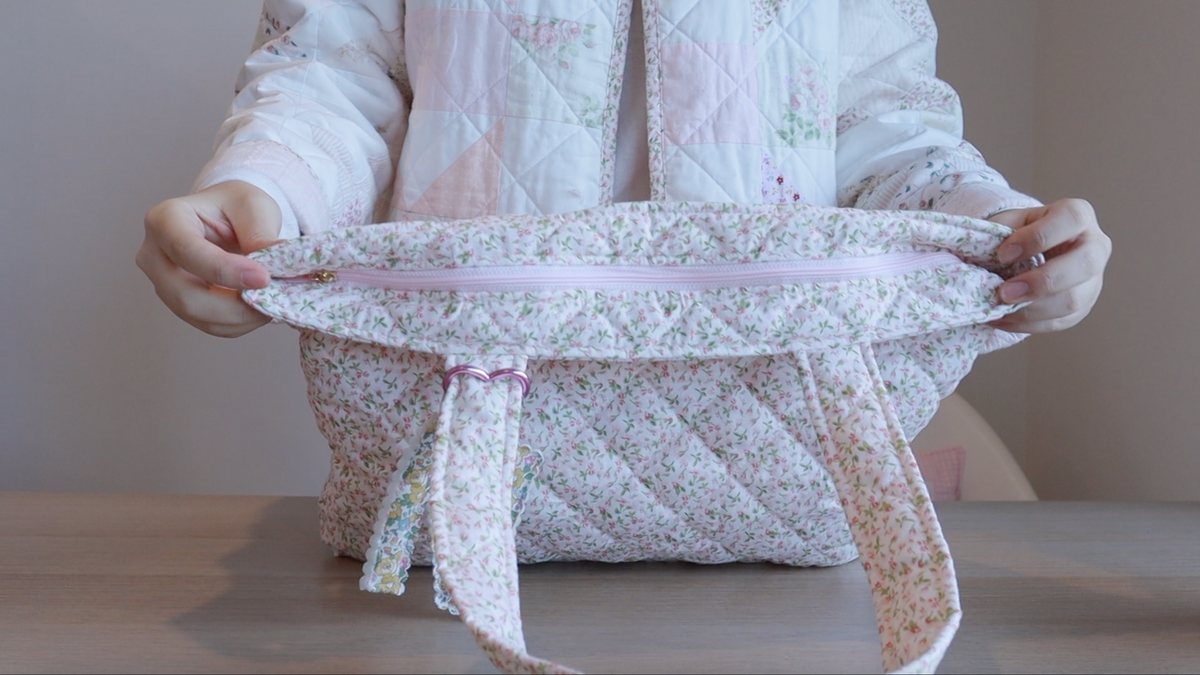 A zippered quilted tote bag with a floral print pattern. The bag features a light pink zipper and matching floral fabric handles.